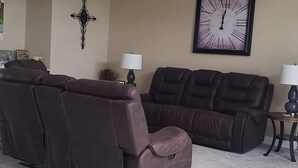 A living room with two brown leather sofas, a ceiling fan, a wall clock, and a small table with a lamp. - Charming 4-bedroom house with AC in lovely Meraux (Meraux)