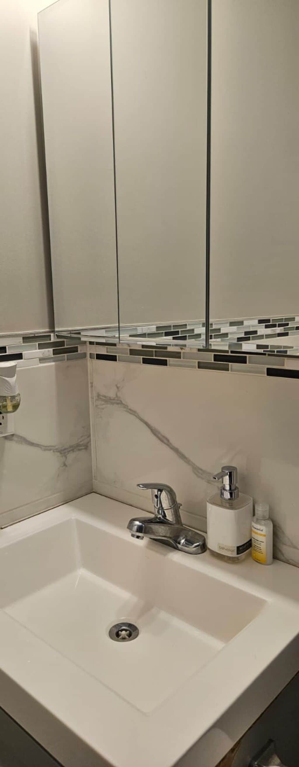 Une salle de bain avec un lavabo blanc, un miroir et un mur recouvert de carreaux.