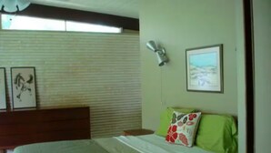 A bedroom with a bed, a nightstand, a wall-mounted lamp, and a framed picture.