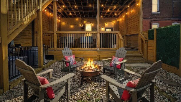 Una terraza de madera con un brasero y cuatro sillas Adirondack, rodeada de un patio de piedra.
