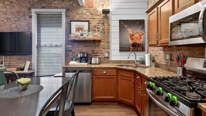 Una cocina moderna con pared de ladrillo, armarios de madera, estufa de acero inoxidable y un comedor con mesa y sillas.