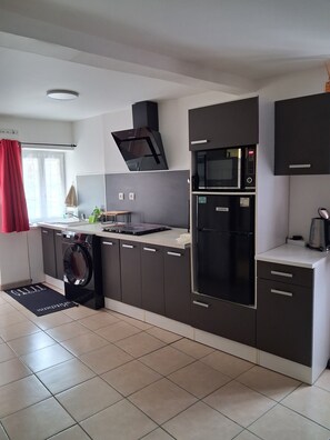 A modern kitchen with a built-in washing machine, a microwave, and a refrigerator. - Cozy Little House   (Veaugues)