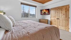 Una camera da letto con un letto grande, una finestra vista alberi, un armadio in legno e un quadro raffigurante un fuoco.
