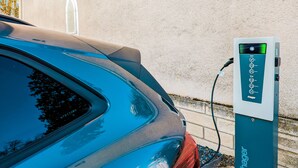 A car parked at an electric charging station with a clear view of the charging interface and a building in the background. - La Laverie (Dosches)