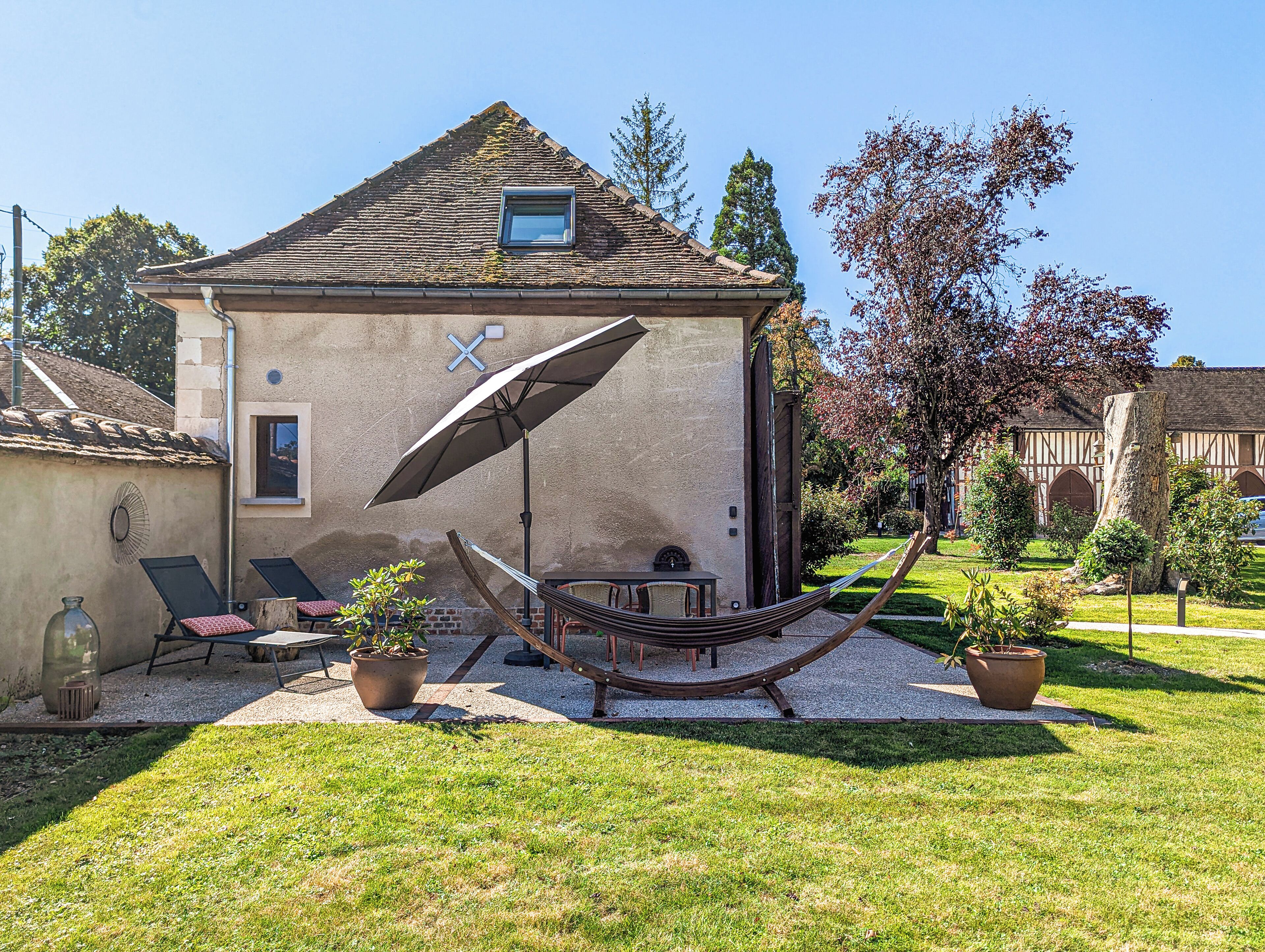 A house with a sloped roof, a hammock, lounge chairs, and potted plants.