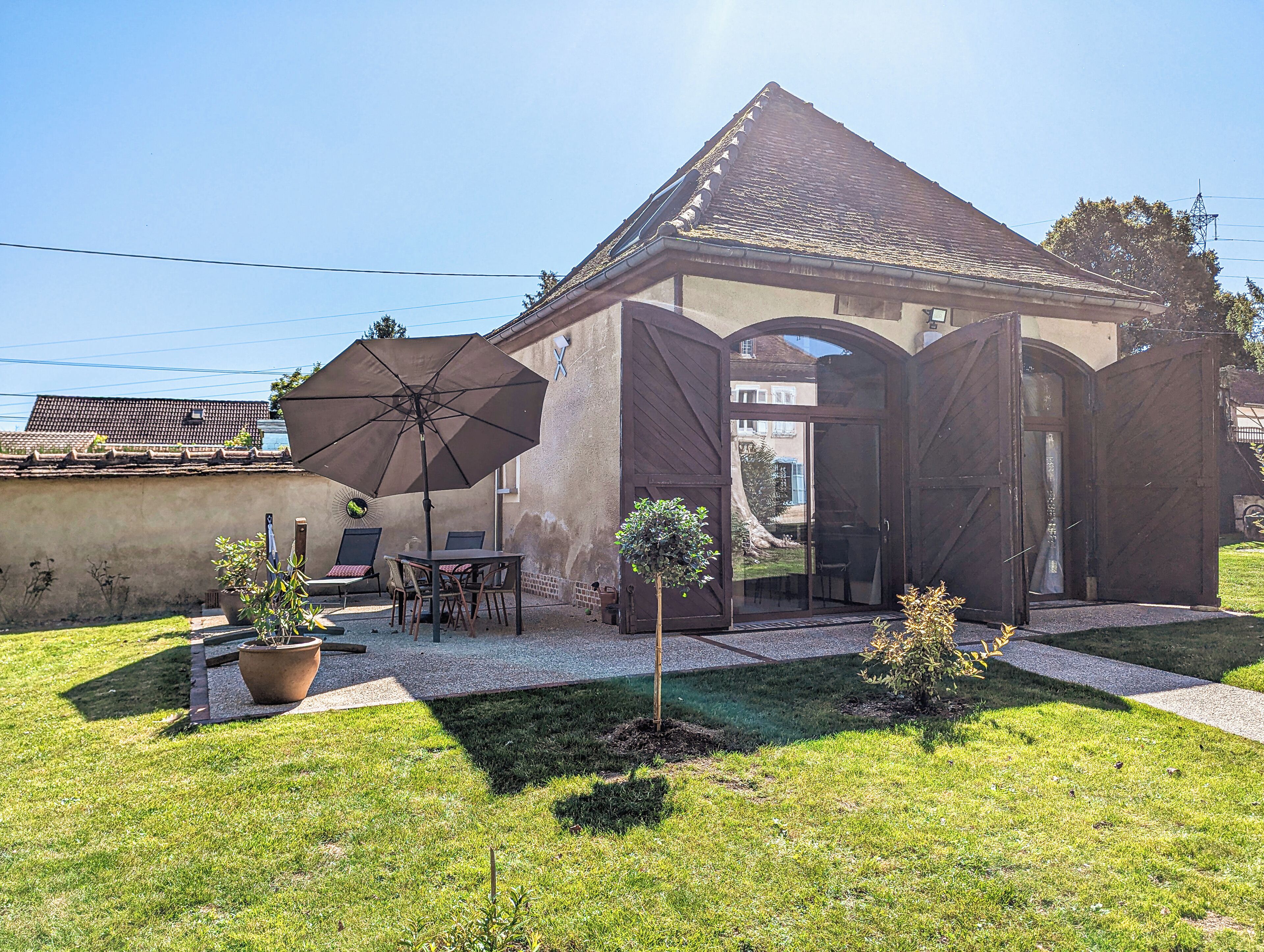 Une maison avec un patio, une table, des chaises, un parasol et des plantes en pot.