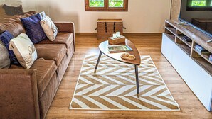 A living room with a brown leather sofa, a coffee table, a TV stand, and a window with a view of greenery. - La Maison T&M: The stable (Dosches)