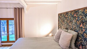 A bedroom with a bed, a window with curtains, and a wall with a floral tapestry. - La Maison T&M: The stable (Dosches)