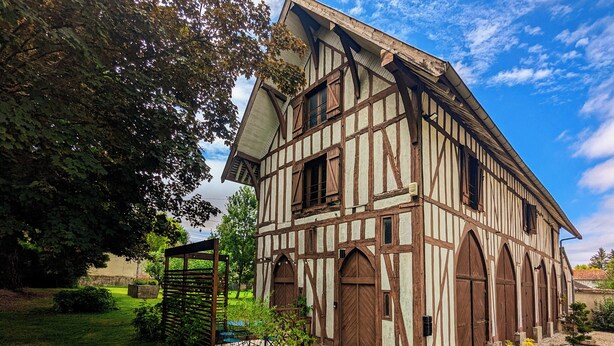 A traditional half-timbered building with a gravel driveway, a wooden gate, and potted plants. - La Maison T&M: The stable (Dosches)