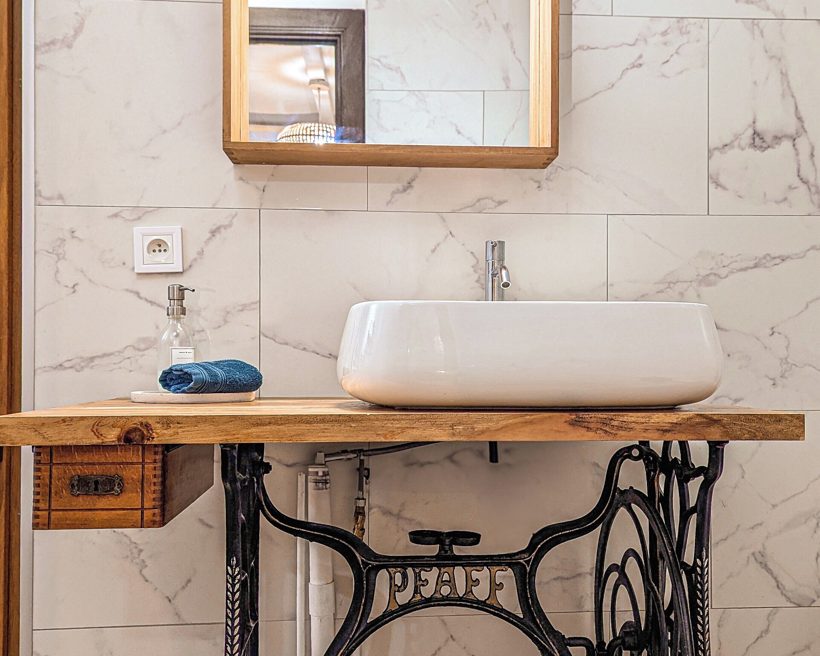 Une salle de bain avec un mur en marbre, un meuble-lavabo en bois, un lavabo blanc, un miroir et un robinet de style vintage.