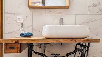 Une salle de bain avec un mur en marbre, un meuble-lavabo en bois, un lavabo blanc, un miroir et un robinet de style vintage.