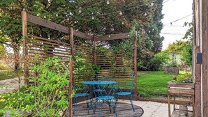 A wooden pergola with blue chairs and a table, surrounded by greenery and a garden. - La Maison T&M: The stable (Dosches)