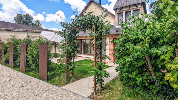 A residential property with a brick house, a wooden pergola, and a gravel pathway. - La Maison T&M: Le Pigeonnier (Dosches)