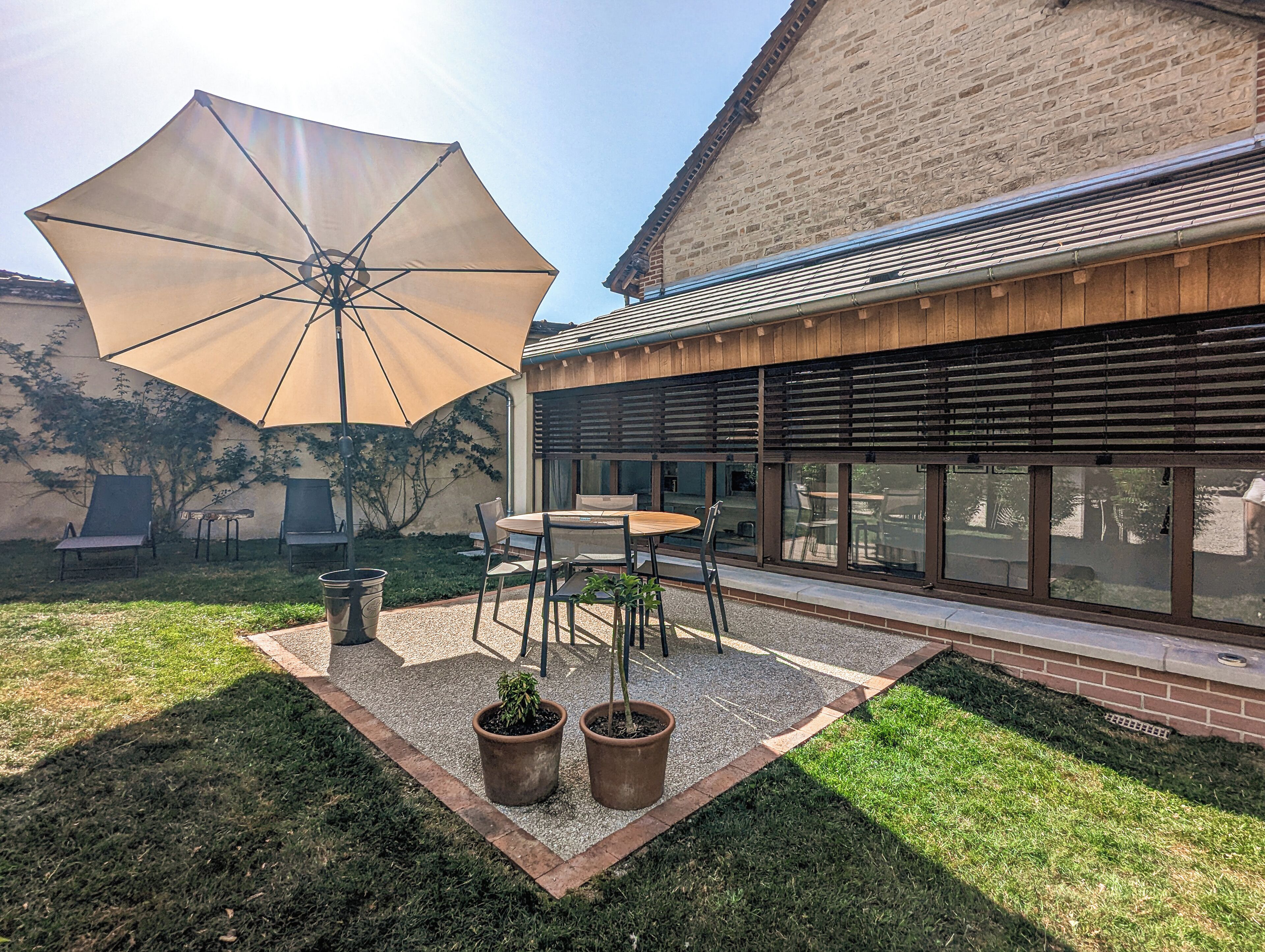 An outdoor patio with a table, chairs, a large umbrella, and potted plants.