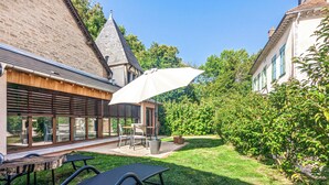 A patio with a table and chairs, a lounge chair, and a large umbrella. - La Maison T&M: Le Pigeonnier (Dosches)