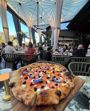 Uma área de refeições ao ar livre com uma pizza em uma tábua de madeira.