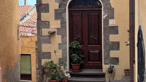 Una calle estrecha con un edificio de fachada de piedra, una puerta de madera con adornos tallados y plantas en macetas en la entrada.