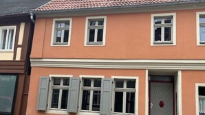 A two-story building with a peach-colored facade, white trim, and multiple windows with shutters. - Beautiful apartment on the ground floor, best city center location near the market square, with own parking space (Stendal)