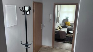 A hallway with a coat rack, a wooden door, and a view into a living room with a sofa and a chair. - Beautiful apartment on the ground floor, best city center location near the market square, with own parking space (Stendal)