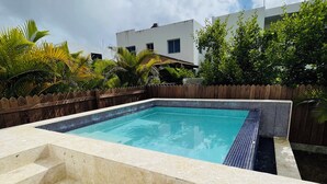 Piscina com escadas de acesso, cercada por um muro de madeira e vegetação.