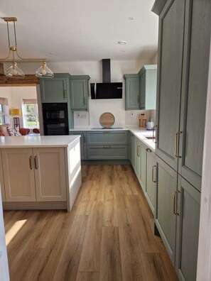 A modern kitchen with light green cabinets, a central island, and a built-in oven. - Luxurious 4-bedroom house perfect for relaxing stays in Cong (Cong)