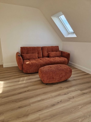 A modern living room with a brown sofa and ottoman, wooden flooring, and a skylight. - Luxurious 4-bedroom house perfect for relaxing stays in Cong (Cong)