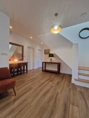 A spacious living area with a wooden floor, a red chair, a table with a lamp, and a ceiling light fixture. - Luxurious 4-bedroom house perfect for relaxing stays in Cong (Cong)