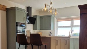 A modern kitchen with a central island, two bar stools, and a large window providing natural light. - Luxurious 4-bedroom house perfect for relaxing stays in Cong (Cong)