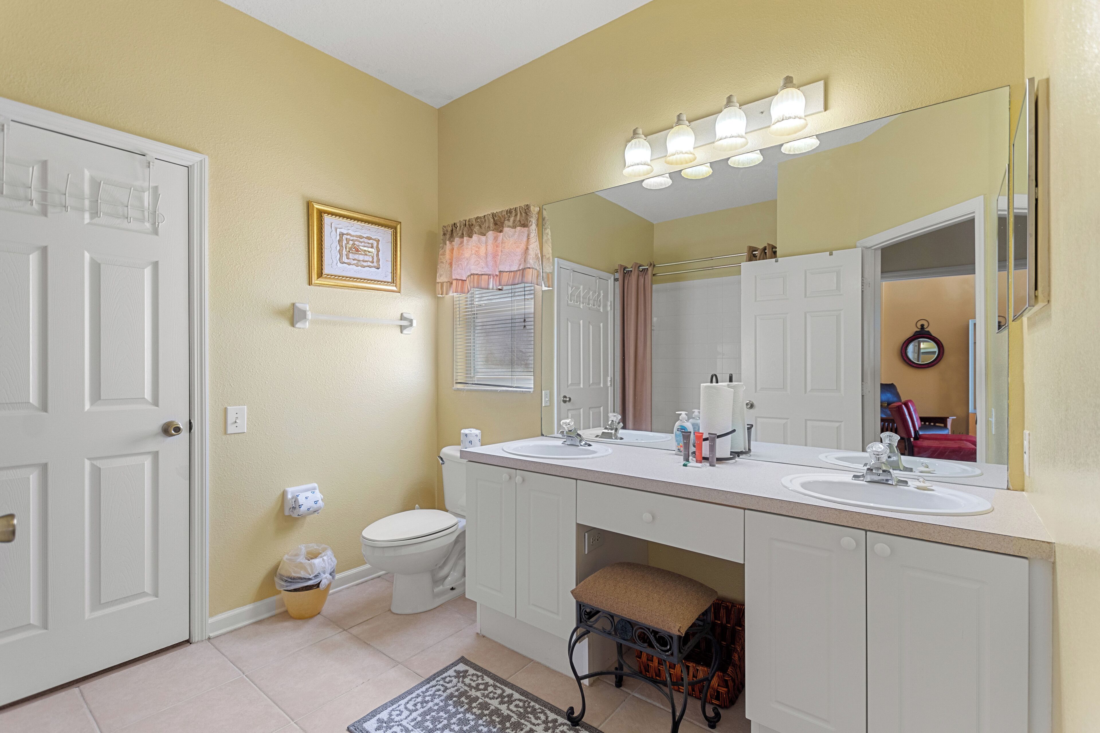 A bathroom with two sinks, a toilet, a mirror, and a rug on the floor.