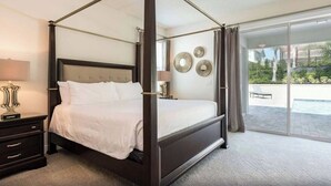 A four-poster bed with a dark wood frame and white bedding, a nightstand with a lamp, and a view of a balcony with outdoor furniture. - 25% Off 9BR Mansion-Pool/Spa/Games! (Kissimmee)