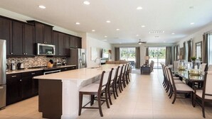 A spacious kitchen with dark cabinets, a large island, and a dining area with chairs. - 25% Off 9BR Mansion-Pool/Spa/Games! (Kissimmee)