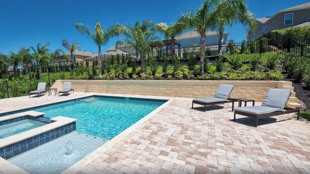 A rectangular swimming pool with a hot tub, surrounded by a brick patio and lounge chairs. - 25% Off 9BR Mansion-Pool/Spa/Games! (Kissimmee)