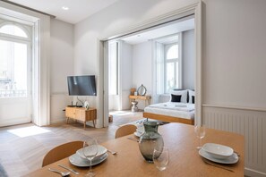 A modern hotel room with a large bed, a TV, a dining area with a table set for two, and a view of the city through the windows. - Gozsdu Panzió (Budapest)