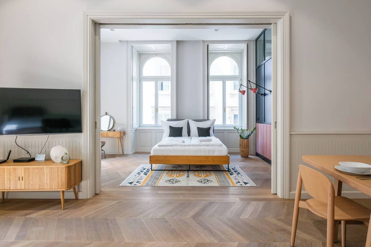 A modern bedroom with a large bed, a TV, a desk, and a dining area.