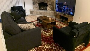 Un salon avec une cheminée en pierre, un téléviseur et des canapés noirs.