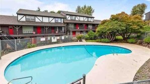 Une piscine à bord incurvé, un bâtiment doté d’un balcon et un arbre en arrière-plan.
