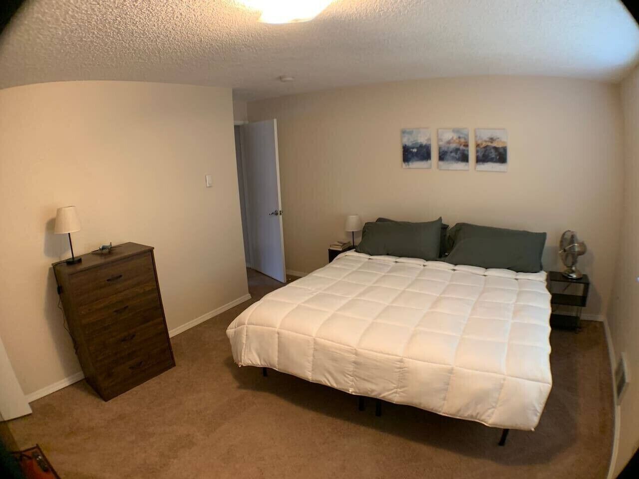 A bedroom with a bed, dresser, nightstands, and wall art.