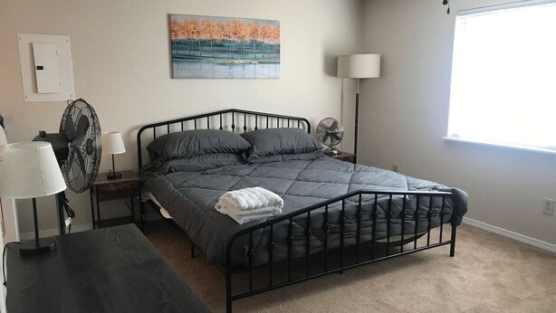 Une chambre à coucher avec un lit, des tables de chevet, une lampe, un ventilateur et un tableau au mur.