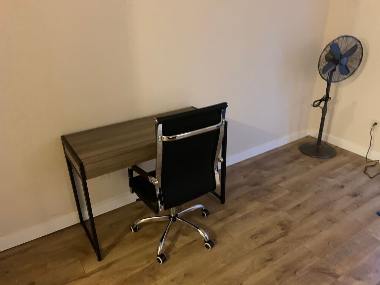 Une pièce avec un bureau en bois et un fauteuil de bureau noir à roulettes.