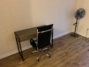 A room with a wooden desk and a black office chair with wheels.