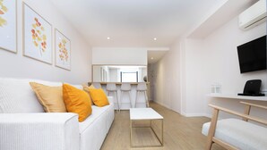 Een moderne woonkamer met een witte bank, een salontafel en een aan de muur bevestigde televisie.
