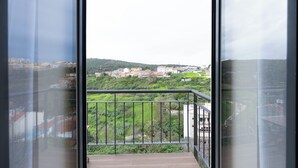 Een balkon met een metalen hekwerk met uitzicht op een groen landschap en gebouwen in de verte.
