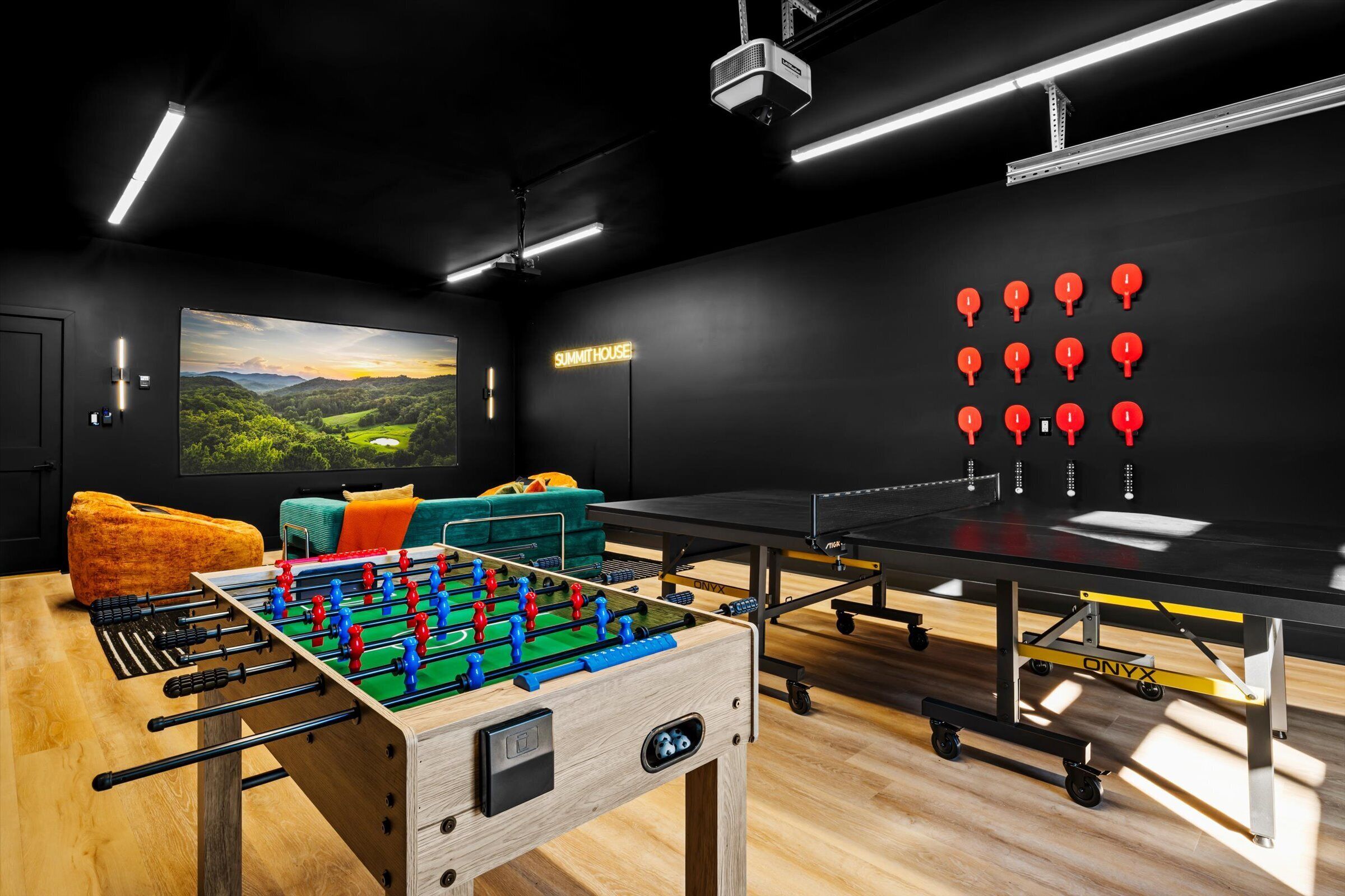 A modern room with a foosball table, a ping pong table, and a large TV screen displaying a scenic landscape.