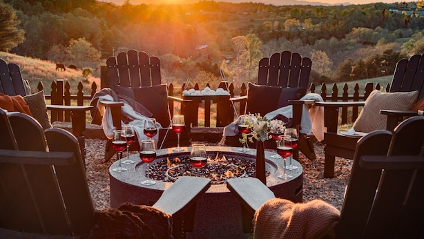 A circular outdoor seating area with Adirondack chairs, a fire pit, and glasses of red wine.