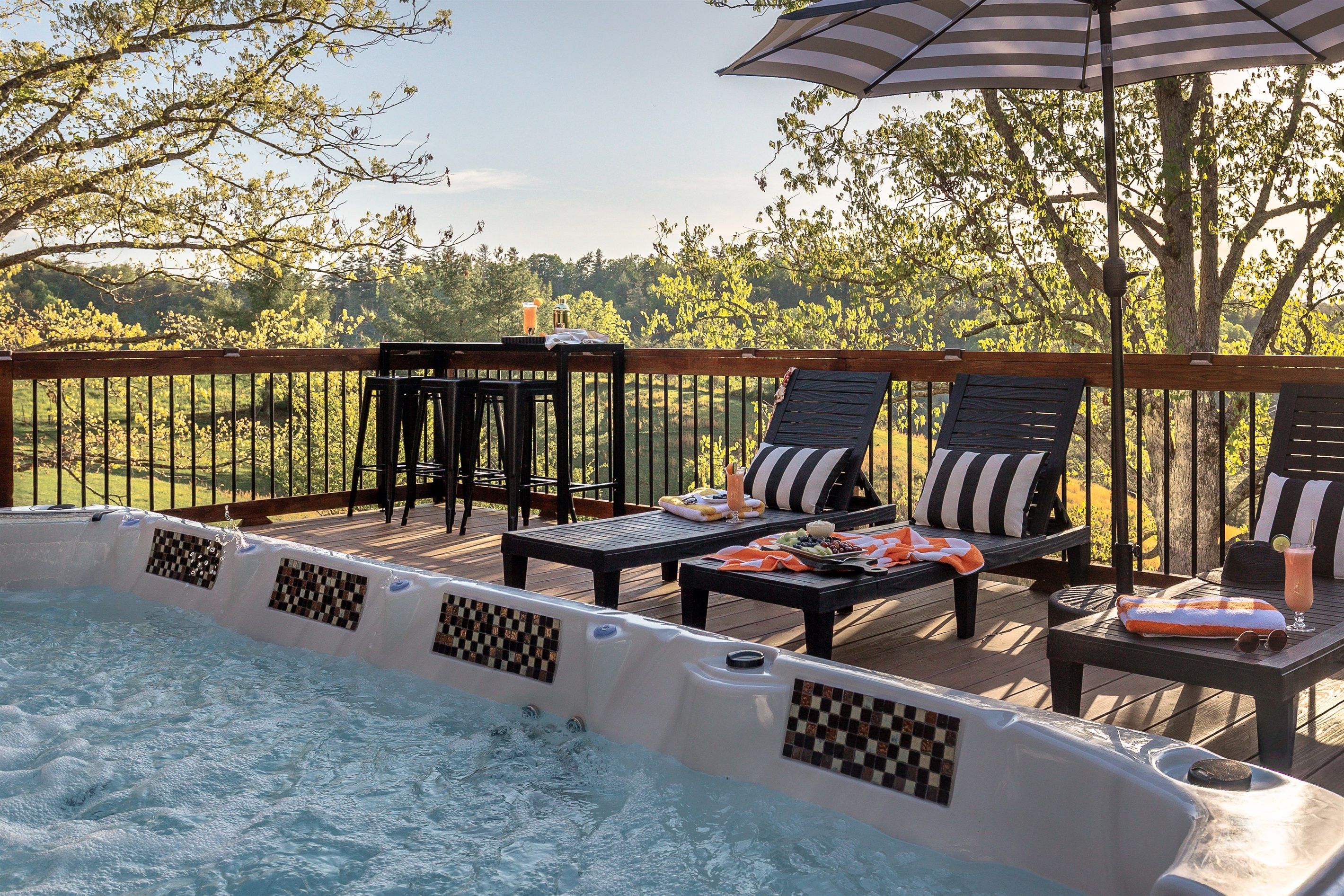 A hot tub with checkered tiles, surrounded by a wooden deck with lounge chairs and a table.