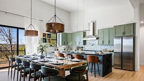 A modern kitchen with green cabinets, a stainless steel refrigerator, and a dining area with a wooden table and green chairs.