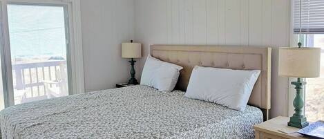 A bedroom with a bed, a nightstand, a lamp, a ceiling fan, and a window with blinds.