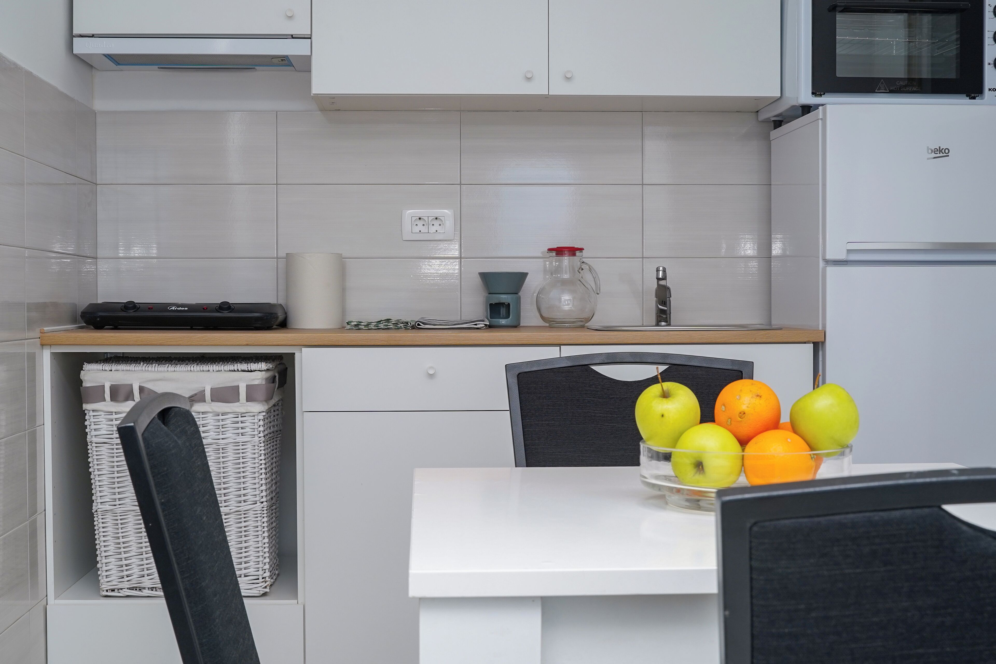 Una cocina moderna con armarios blancos, un microondas, una tetera y un frutero sobre la encimera.