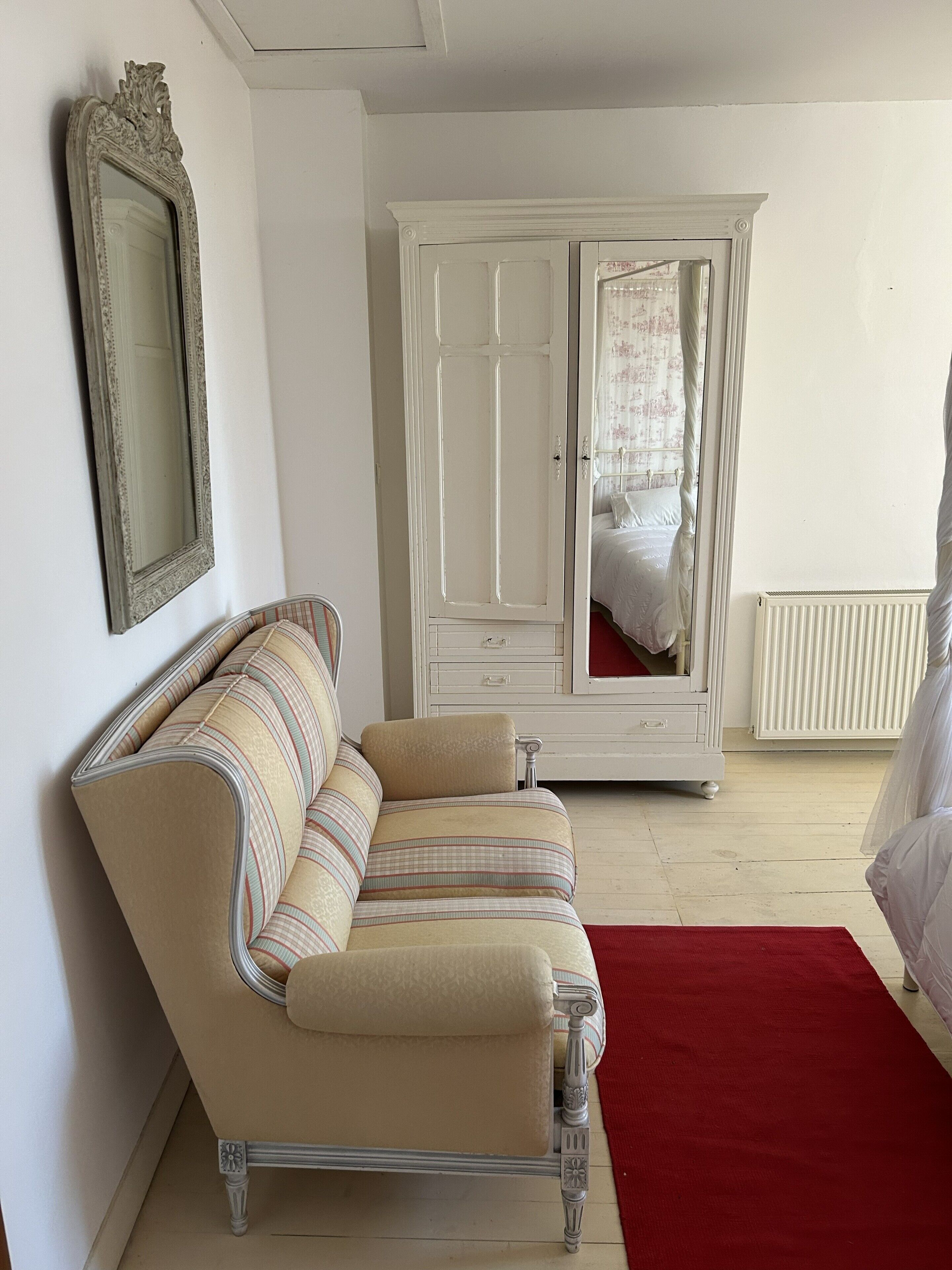 Een kamer met een bank, een garderobe, een spiegel en een bed met een rood vloerkleed.