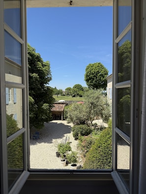 A view through an open window of a courtyard with a gravel path, potted plants, and a small structure. - Charentaise cottage - private swimming pool (Saint-Palais-du-Né)